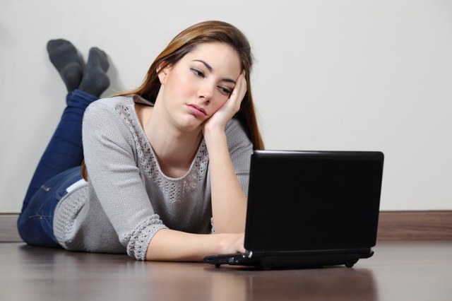 Slika devojke kojoj je dosadno da cita sa laptopa